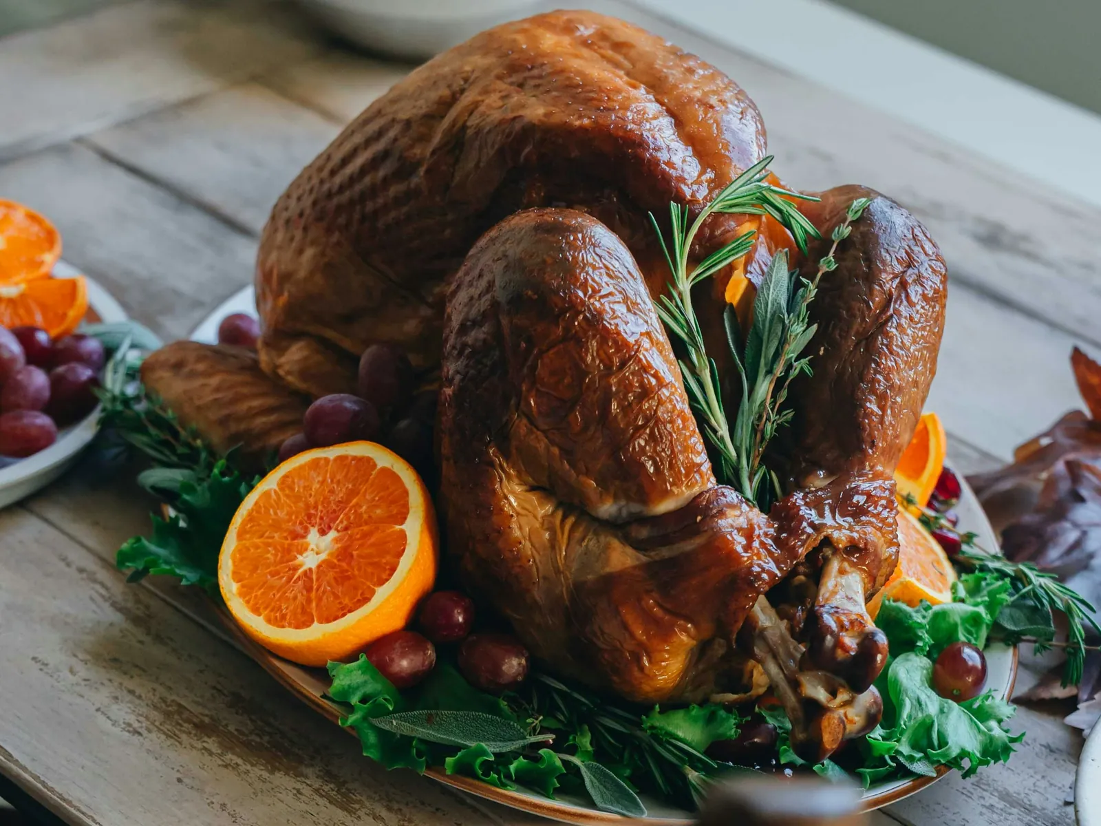 a golden roasted thanksgiving turkey on a platter with orange halves, grapes and fresh rosemary and sage, the centrepiece of a holiday dinner ordered for pickup or delivery in minneapolis